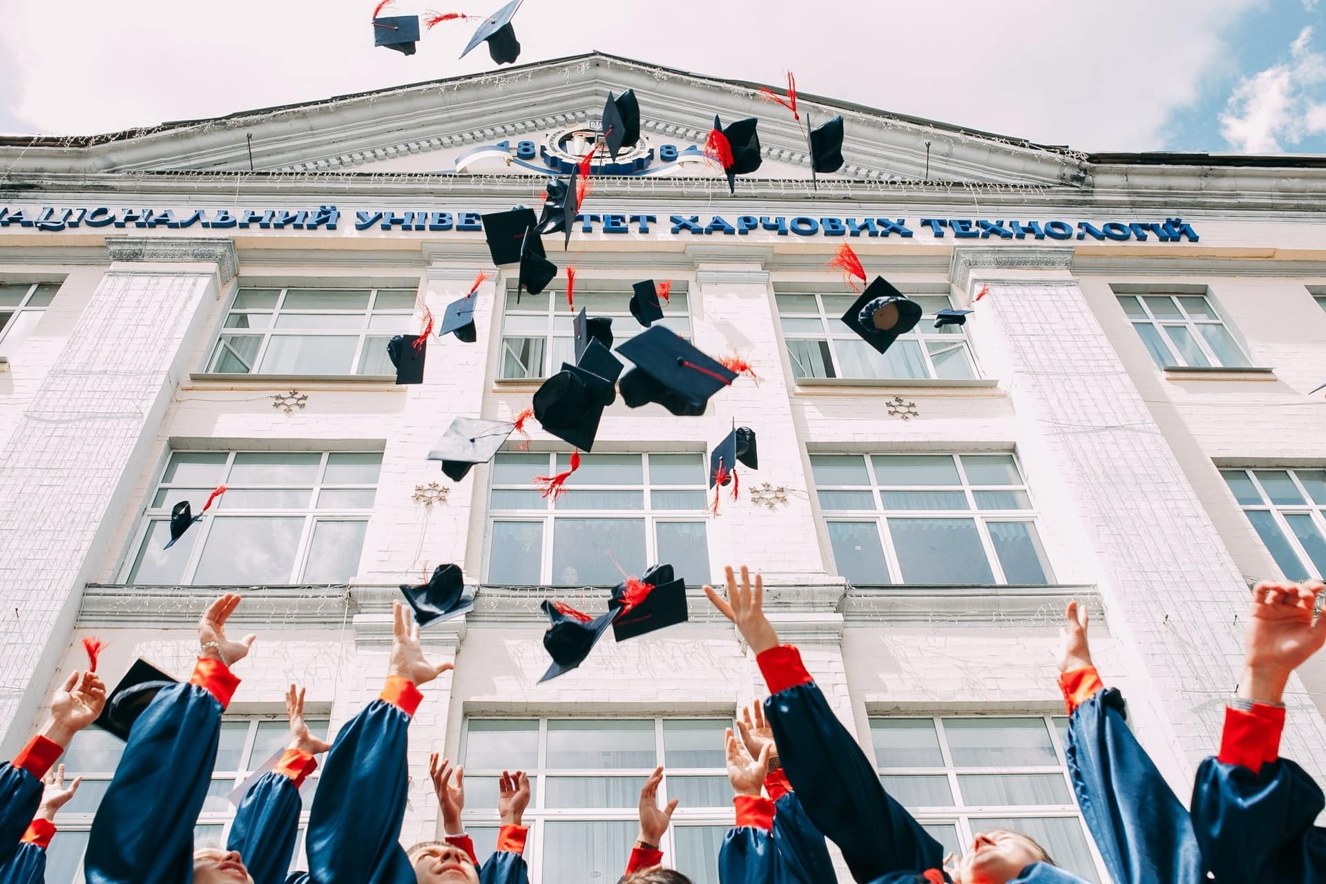 Absolventinnen und Absolventen werfen ihre Hüte vor einem Hochschulgebäude